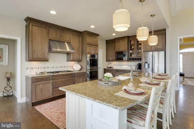 kitchen featuring a center island with sink, decorative light fixtures, appliances with stainless steel finishes, and dark wood-type flooring