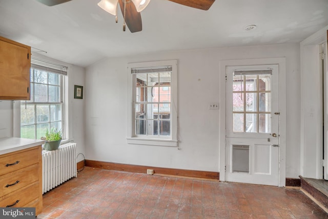 doorway with a wealth of natural light, vaulted ceiling, radiator, and ceiling fan