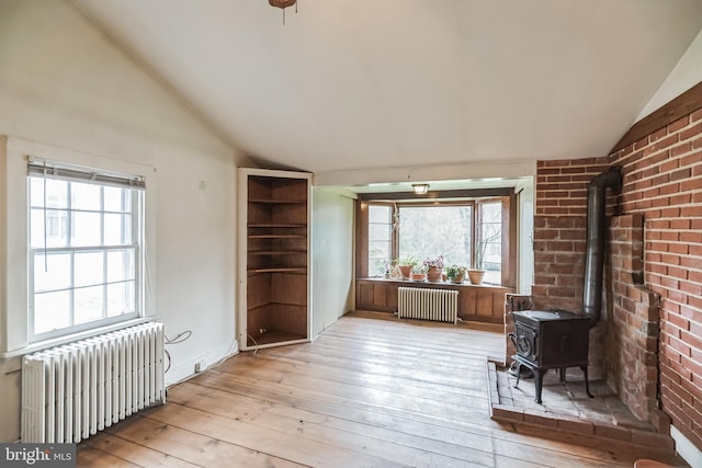 living room featuring a wood stove, radiator heating unit, a healthy amount of sunlight, and light wood-type flooring