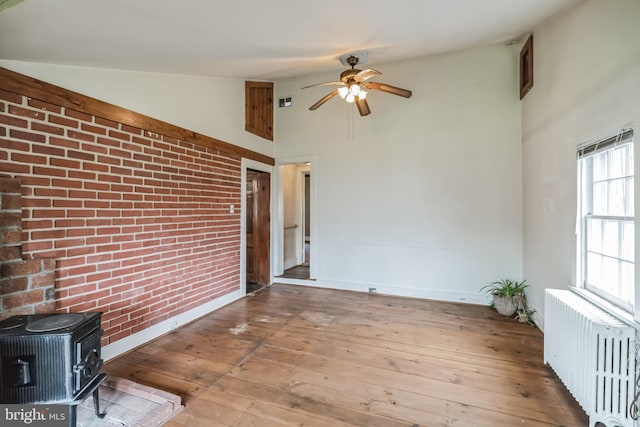 interior space with hardwood / wood-style flooring, vaulted ceiling, radiator heating unit, and a wood stove