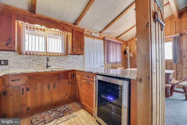 kitchen featuring beverage cooler, lofted ceiling with beams, light carpet, light stone counters, and sink