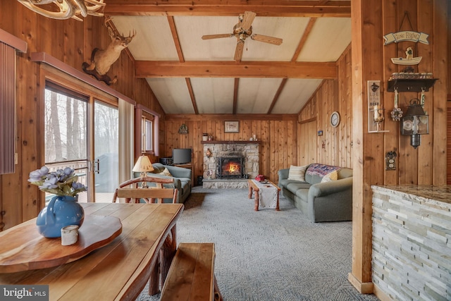 living room with a stone fireplace, dark carpet, and vaulted ceiling with beams