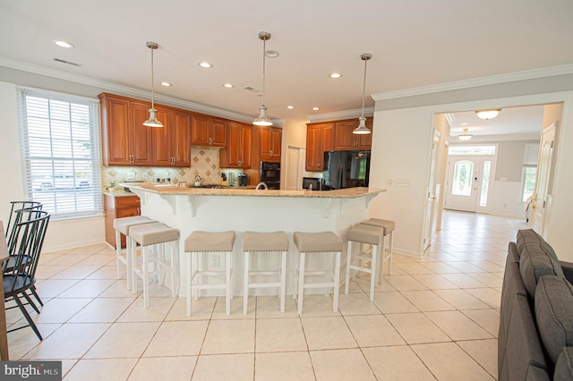 kitchen with a center island with sink, a breakfast bar, black refrigerator, and hanging light fixtures