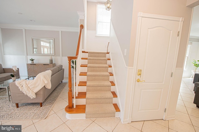 staircase featuring tile patterned floors, a notable chandelier, and ornamental molding