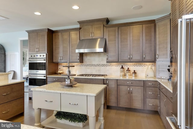 kitchen with dark hardwood / wood-style flooring, tasteful backsplash, stainless steel appliances, light stone countertops, and wall chimney exhaust hood