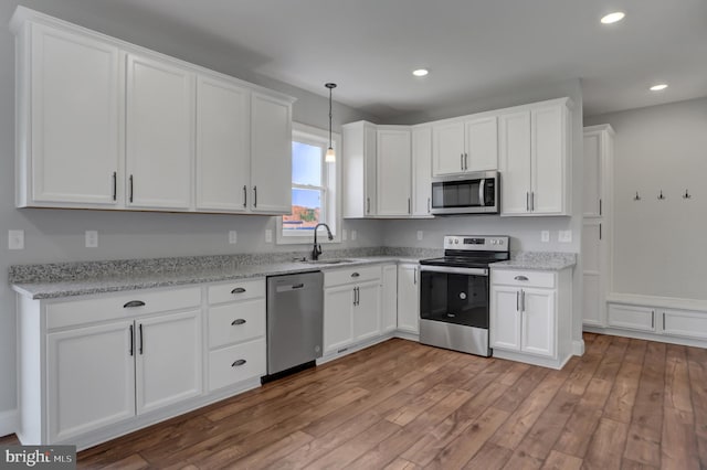 kitchen featuring hardwood / wood-style floors, stainless steel appliances, white cabinets, and decorative light fixtures