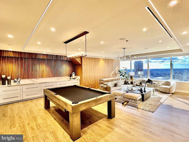 recreation room with wood walls, light wood-type flooring, pool table, and a chandelier