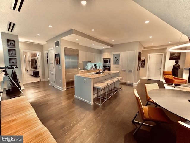 kitchen with a kitchen bar, dark wood-type flooring, appliances with stainless steel finishes, light stone counters, and sink