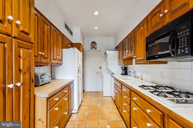 kitchen featuring sink, light tile flooring, a textured ceiling, white gas cooktop, and tasteful backsplash