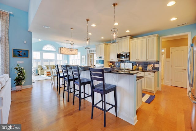 kitchen featuring hanging light fixtures, a breakfast bar, light hardwood / wood-style flooring, a kitchen island, and tasteful backsplash