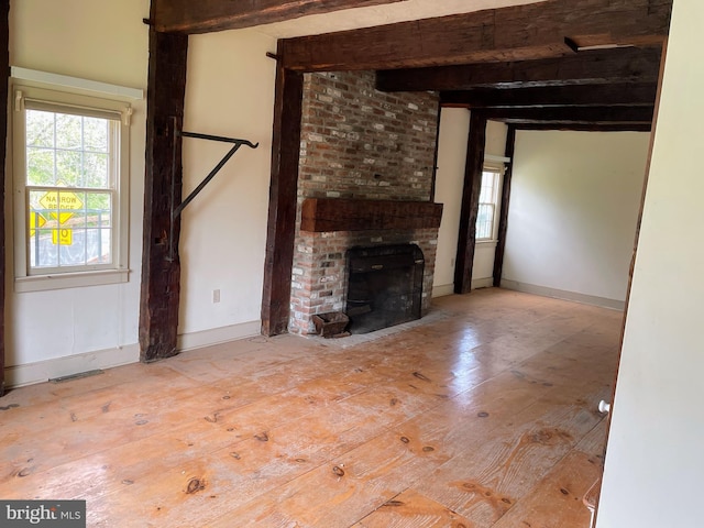 unfurnished living room with beamed ceiling, light wood-type flooring, and a brick fireplace