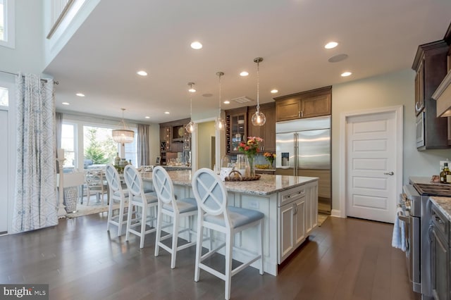 kitchen featuring built in appliances, decorative light fixtures, dark wood-type flooring, and a center island