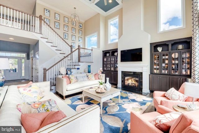 living room with a towering ceiling, ornamental molding, an inviting chandelier, and wood-type flooring