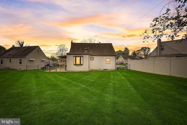 back house at dusk with a lawn and a patio area