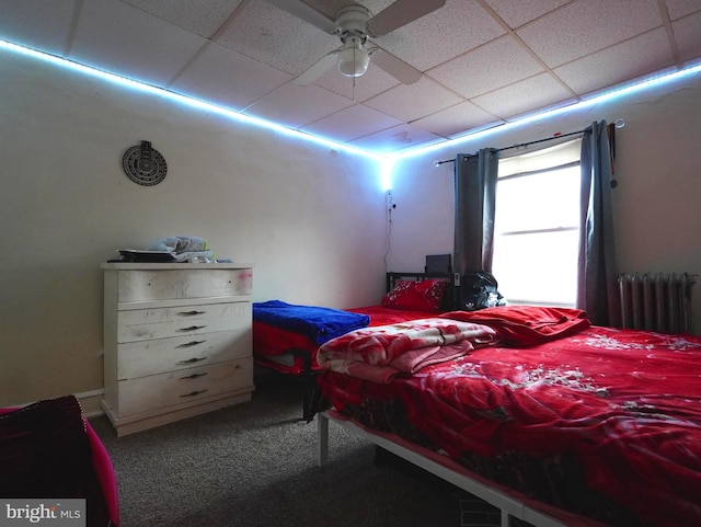 bedroom featuring ceiling fan, a paneled ceiling, dark carpet, and radiator heating unit