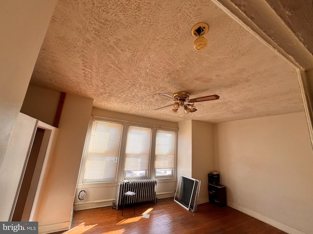 interior space with wood-type flooring, ceiling fan, radiator heating unit, and a textured ceiling