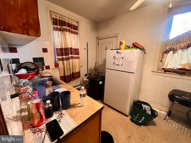 kitchen with white fridge, sink, light tile floors, and tile walls