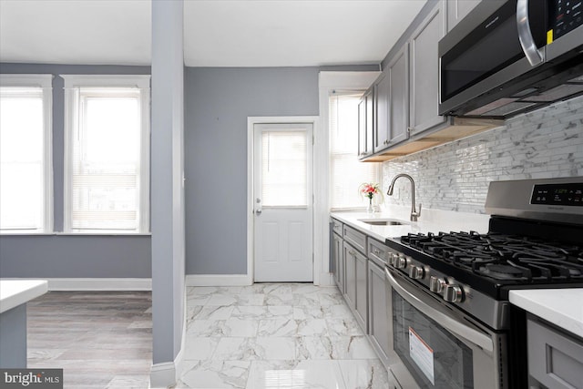 kitchen featuring tasteful backsplash, light tile floors, stainless steel appliances, gray cabinets, and sink