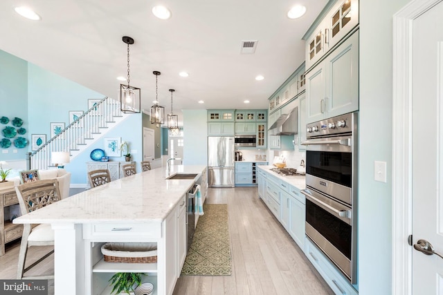 kitchen featuring a kitchen island with sink, a kitchen bar, light hardwood / wood-style flooring, stainless steel appliances, and pendant lighting