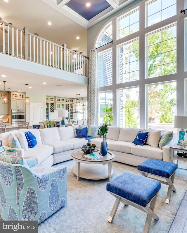 living room featuring coffered ceiling, crown molding, a towering ceiling, and an inviting chandelier