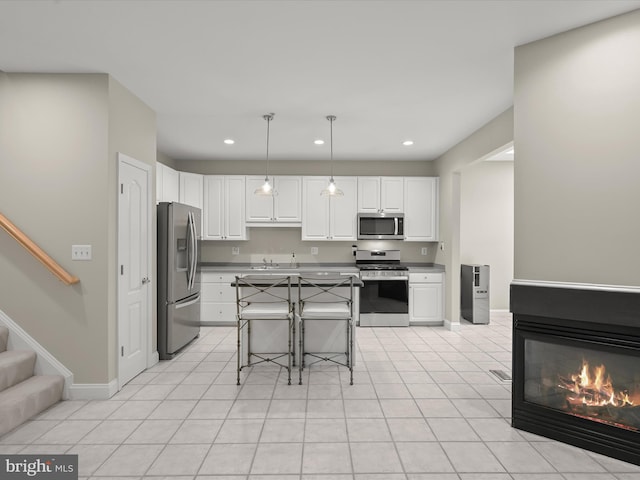 kitchen with a breakfast bar area, appliances with stainless steel finishes, a multi sided fireplace, white cabinets, and decorative light fixtures