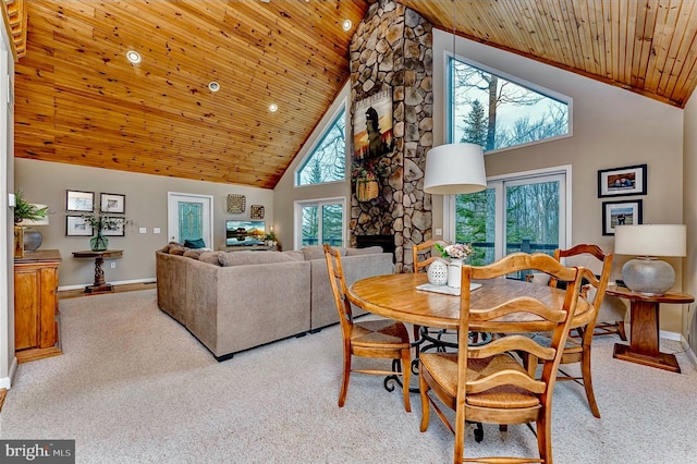 dining area featuring high vaulted ceiling, wood ceiling, light carpet, and a stone fireplace