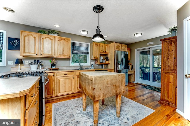 kitchen featuring stainless steel appliances, sink, a textured ceiling, light hardwood / wood-style floors, and hanging light fixtures