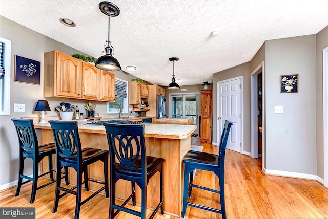 kitchen featuring hanging light fixtures, light hardwood / wood-style flooring, a kitchen bar, and kitchen peninsula