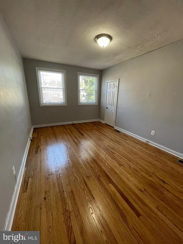 unfurnished room with a textured ceiling and wood-type flooring