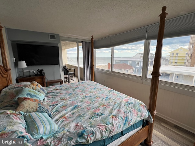 bedroom featuring a water view, light wood-type flooring, and a textured ceiling