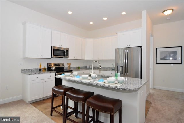 kitchen with stainless steel appliances, light stone countertops, light carpet, a center island with sink, and white cabinets