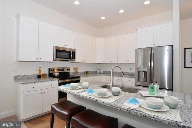 kitchen with appliances with stainless steel finishes, light stone counters, white cabinetry, a kitchen bar, and sink