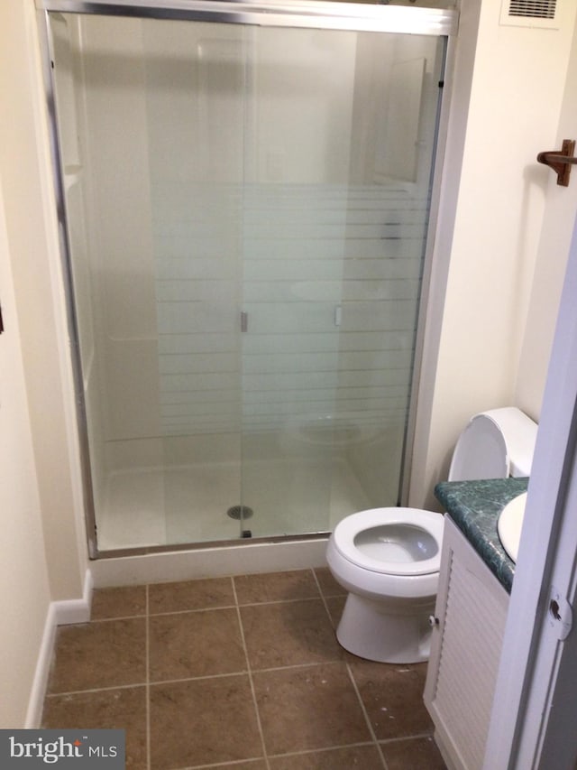 bathroom with tile flooring, toilet, vanity, and a shower with shower door