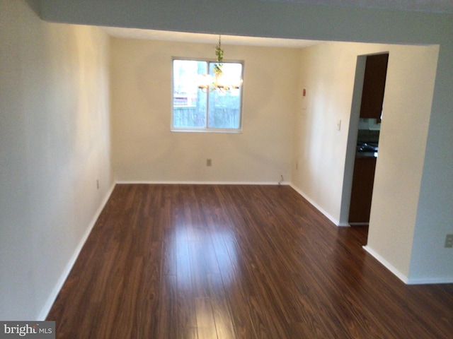 unfurnished room with an inviting chandelier and dark wood-type flooring