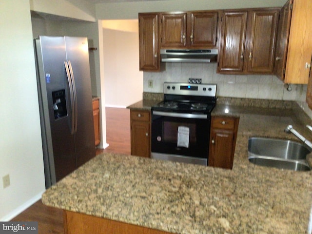 kitchen with light stone countertops, backsplash, range hood, sink, and stainless steel appliances