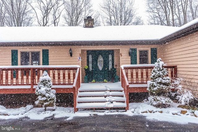 snow covered property entrance with a wooden deck