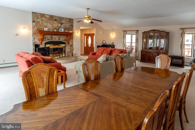 carpeted dining area featuring a baseboard radiator, vaulted ceiling, a stone fireplace, and ceiling fan