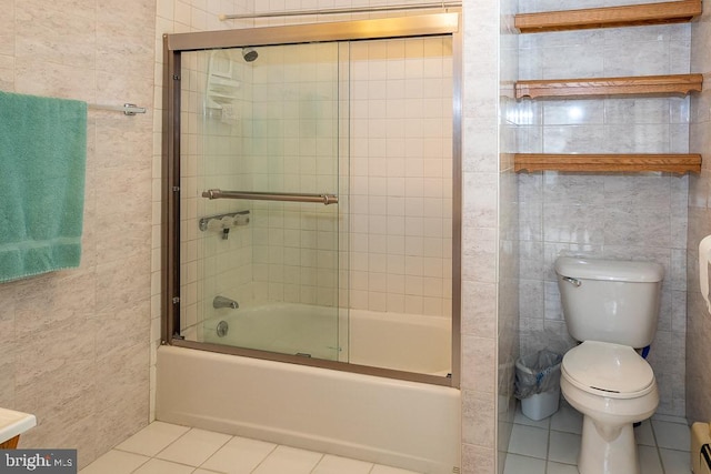 bathroom featuring toilet, combined bath / shower with glass door, tile patterned flooring, and tile walls