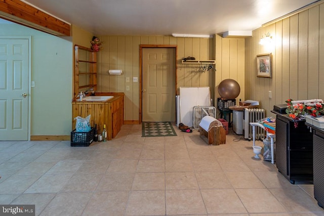 interior space featuring radiator, light tile patterned floors, sink, and wooden walls