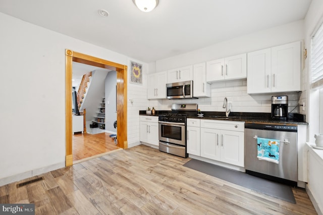 kitchen with stainless steel appliances, white cabinetry, sink, and light wood-type flooring