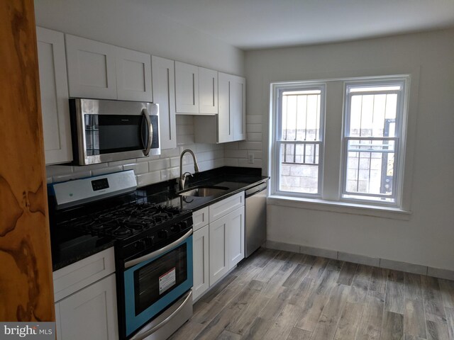 kitchen featuring appliances with stainless steel finishes, light hardwood / wood-style flooring, backsplash, white cabinets, and sink