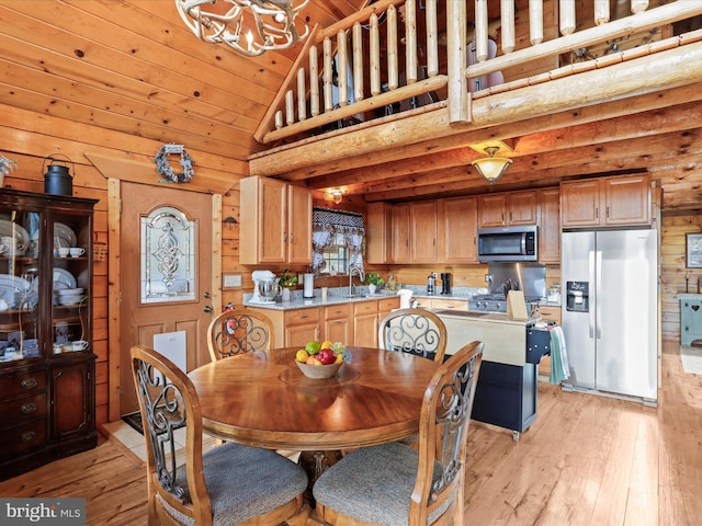 dining area with sink, an inviting chandelier, wood walls, lofted ceiling, and light wood-type flooring