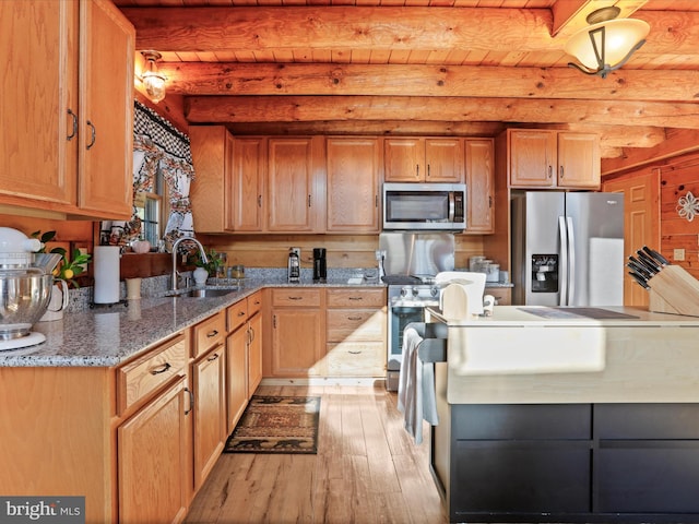 kitchen with beam ceiling, sink, stainless steel appliances, light hardwood / wood-style flooring, and dark stone countertops