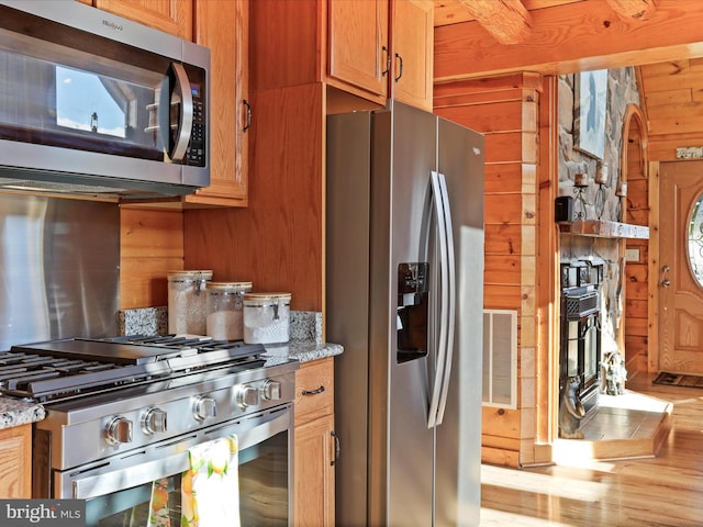 kitchen featuring stainless steel appliances, light hardwood / wood-style flooring, wooden walls, and light stone counters