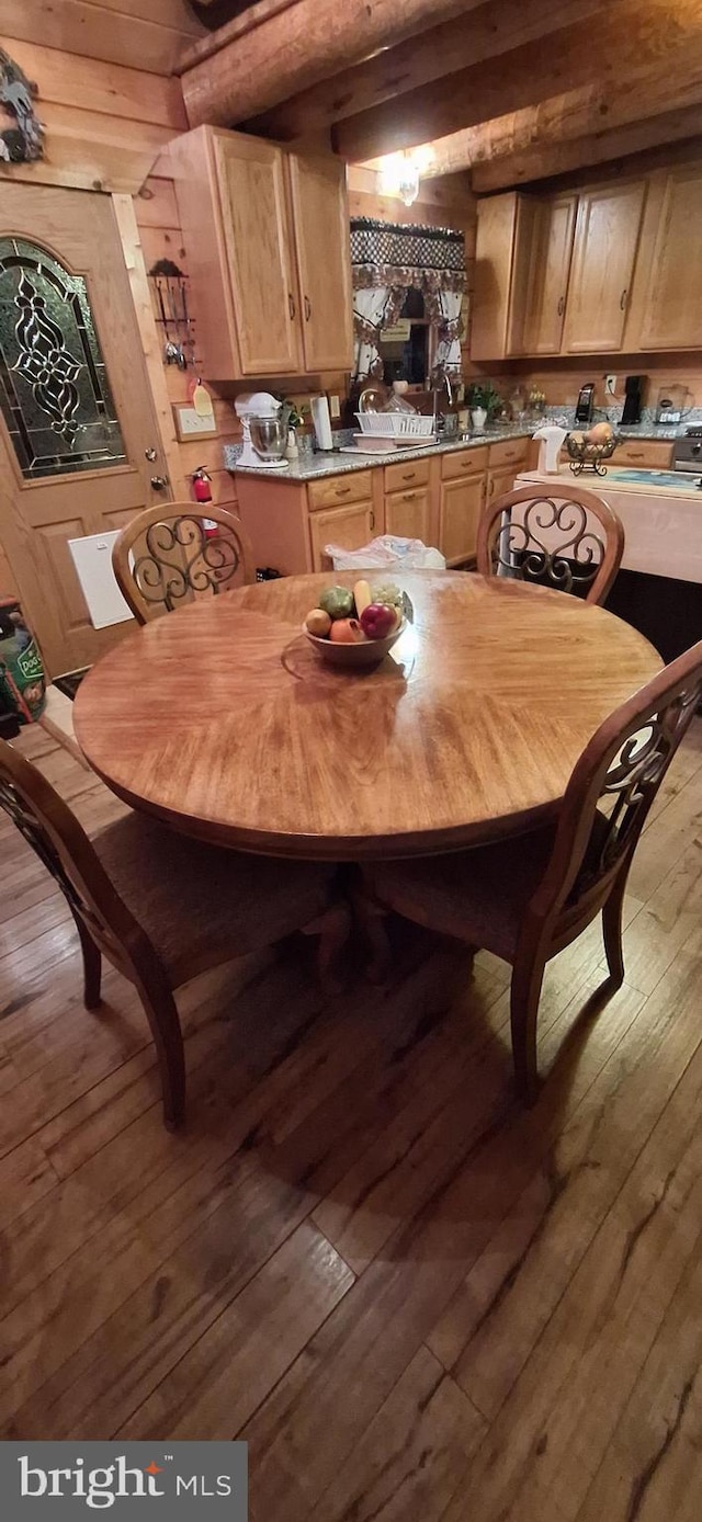 dining area featuring beam ceiling, wood walls, and light hardwood / wood-style flooring