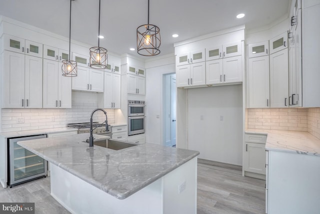 kitchen featuring white cabinets, a kitchen island with sink, decorative light fixtures, and wine cooler