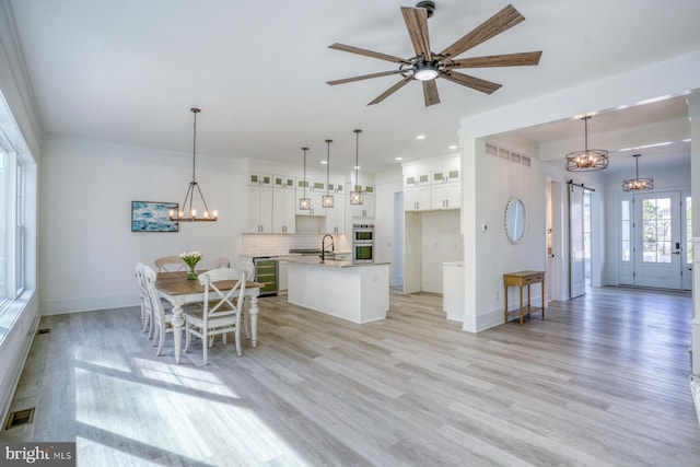 interior space featuring a center island with sink, hanging light fixtures, double oven, white cabinetry, and light hardwood / wood-style flooring