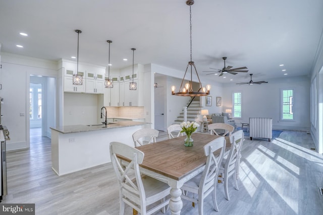 dining area with ceiling fan with notable chandelier, light hardwood / wood-style flooring, and sink