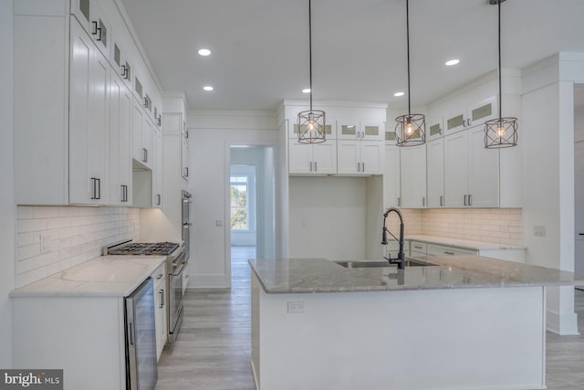 kitchen with a center island with sink, white cabinetry, sink, decorative light fixtures, and light wood-type flooring