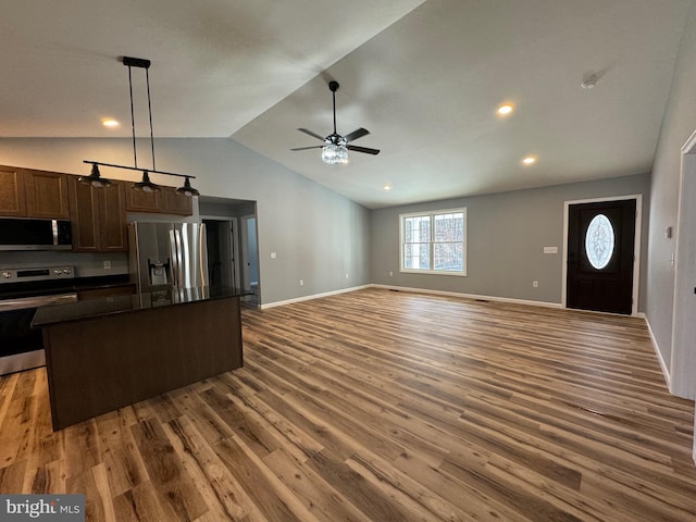 kitchen featuring dark wood-type flooring, lofted ceiling, decorative light fixtures, a kitchen island, and stainless steel appliances